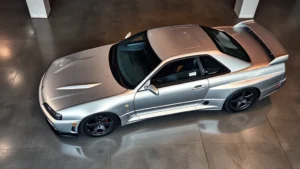 Professional overhead view of a silver Nissan Skyline R34 parked in a modern showroom with polished concrete floors and professional lighting, showing the iconic body lines and twin-turbo badge, photorealistic, clean condition, no signage